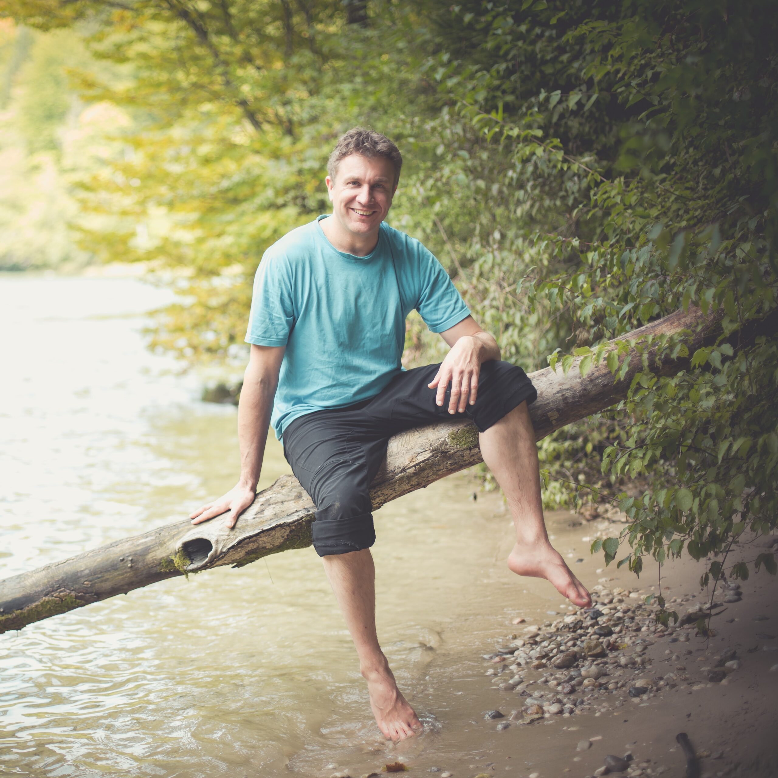 Andreas sitzt auf einem Baumstamm über dem Wasser